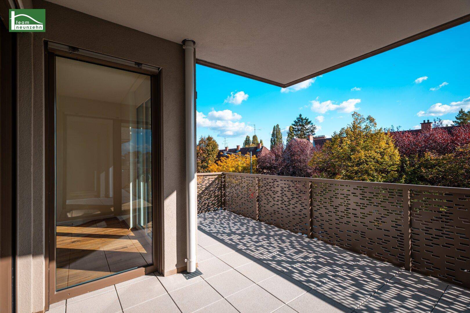 Sonniger Balkon mit Blick auf grüne Bäume und die umliegende Wohngegend.