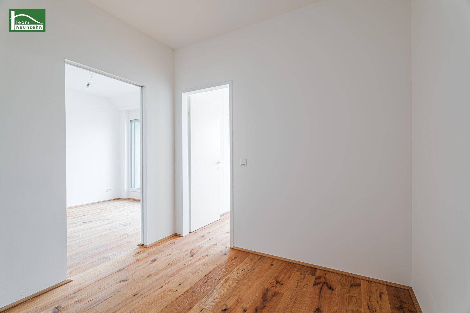 Heller Flur mit Holzboden und weißen Wänden, der zu verschiedenen Zimmern führt.
