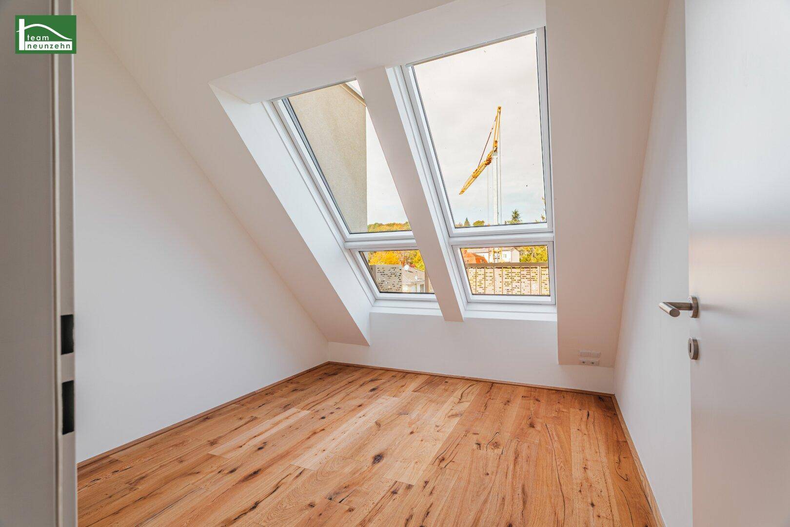 Dachzimmer mit Holzboden und schrägen Wänden, ausgestattet mit großen Dachfenstern für viel Licht.