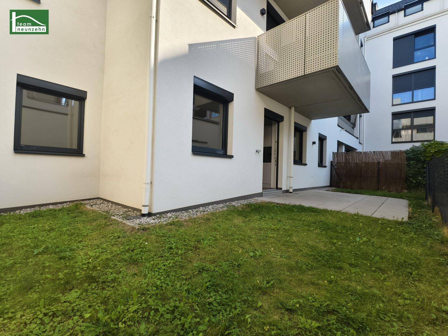 Ruhige Terrasse mit Rasenfläche und Blick auf die moderne Wohnanlage mit Balkonen.