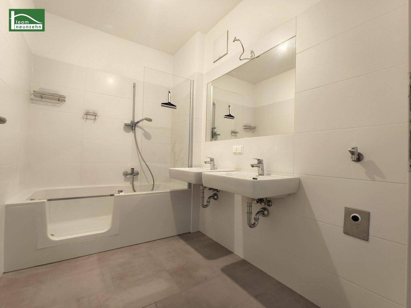 Modernes Badezimmer mit Doppelwaschbecken, Badewanne mit Dusche und großen Wandfliesen.