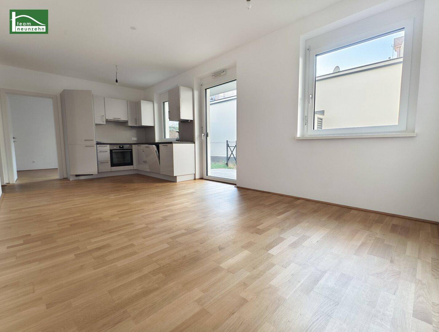 Heller offener Wohn-Essbereich mit integrierter Küche, Parkettboden und Zugang zur Terrasse.