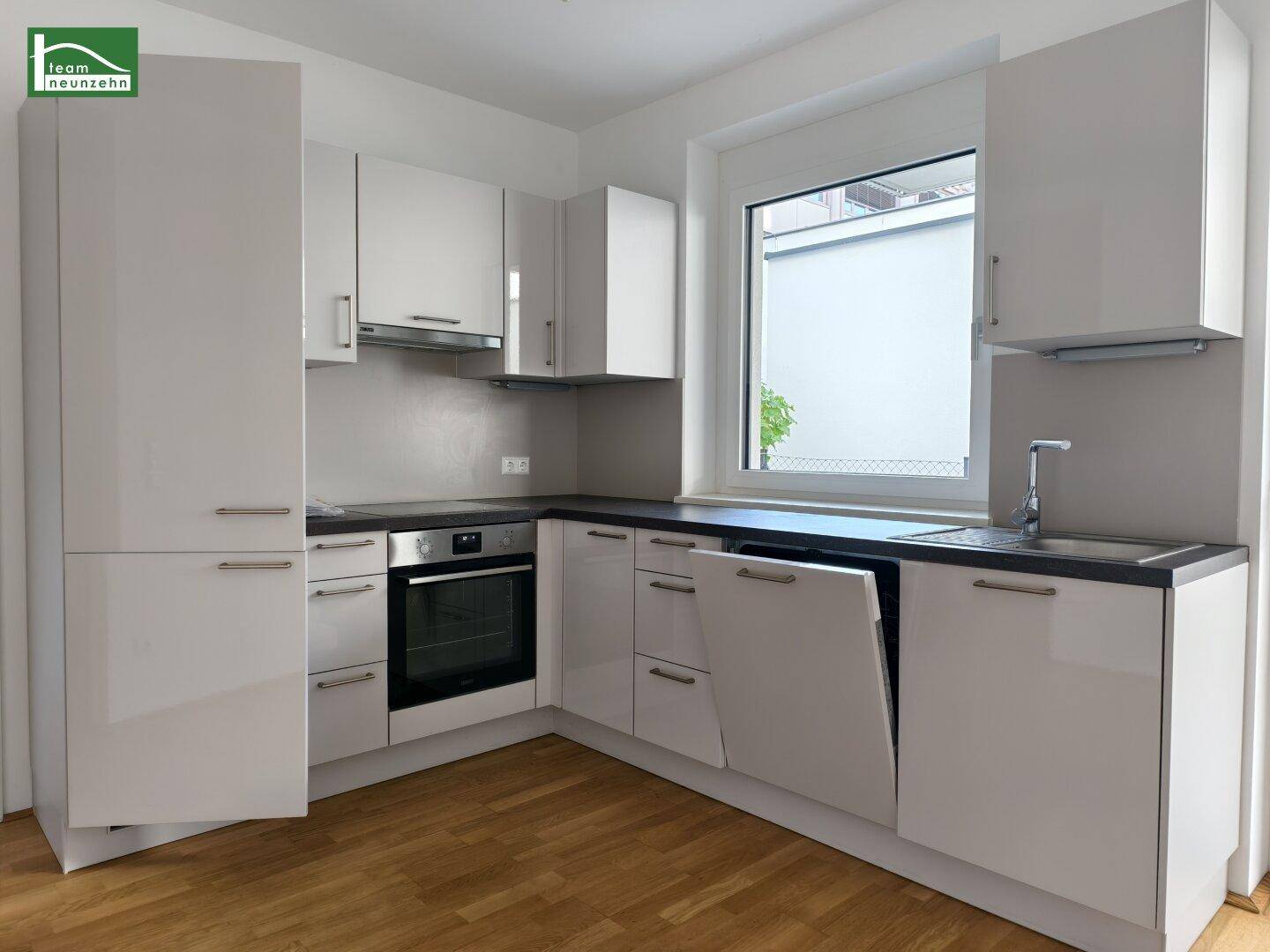 Moderne Einbauküche mit weißen Hochglanzfronten, dunkler Arbeitsplatte und integrierten Geräten.
