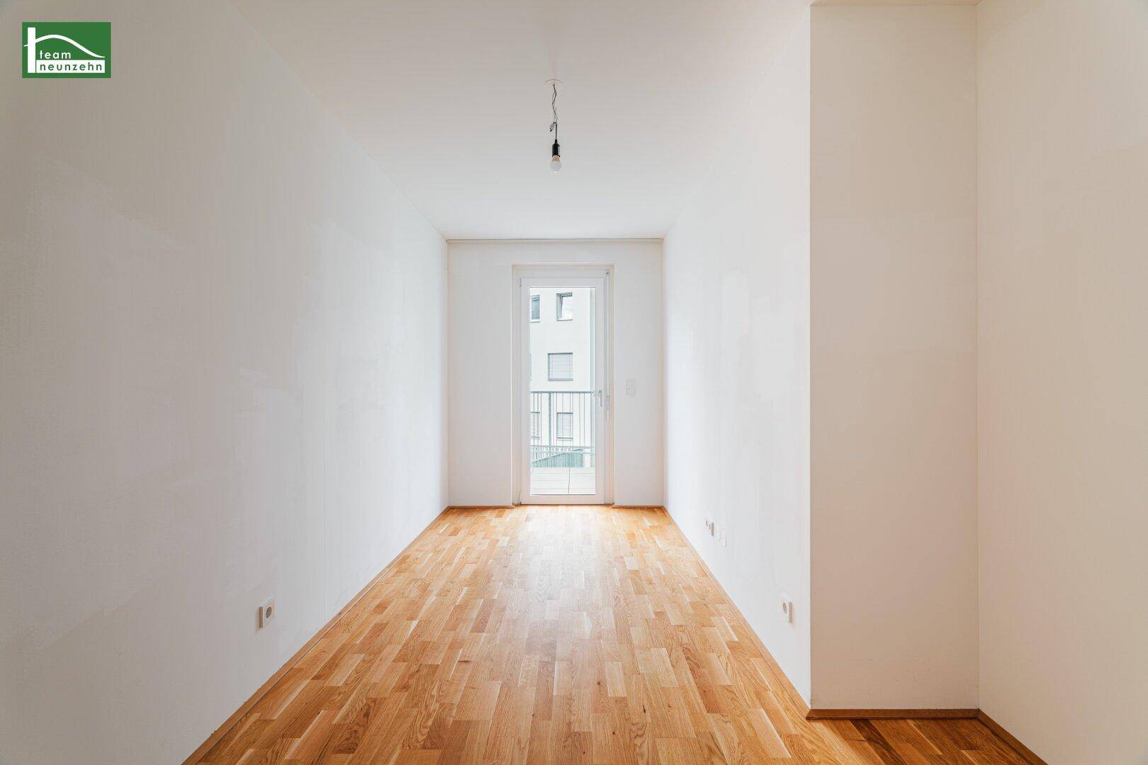 Langes, helles Zimmer mit Parkettboden und Balkonzugang, bietet vielseitige Nutzungsmöglichkeiten.