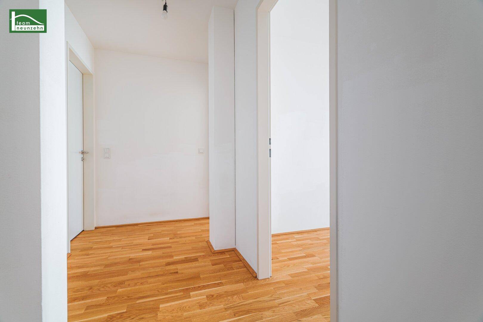 Schmaler, heller Flur mit Holzboden und weißen Wänden, der verschiedene Bereiche verbindet.