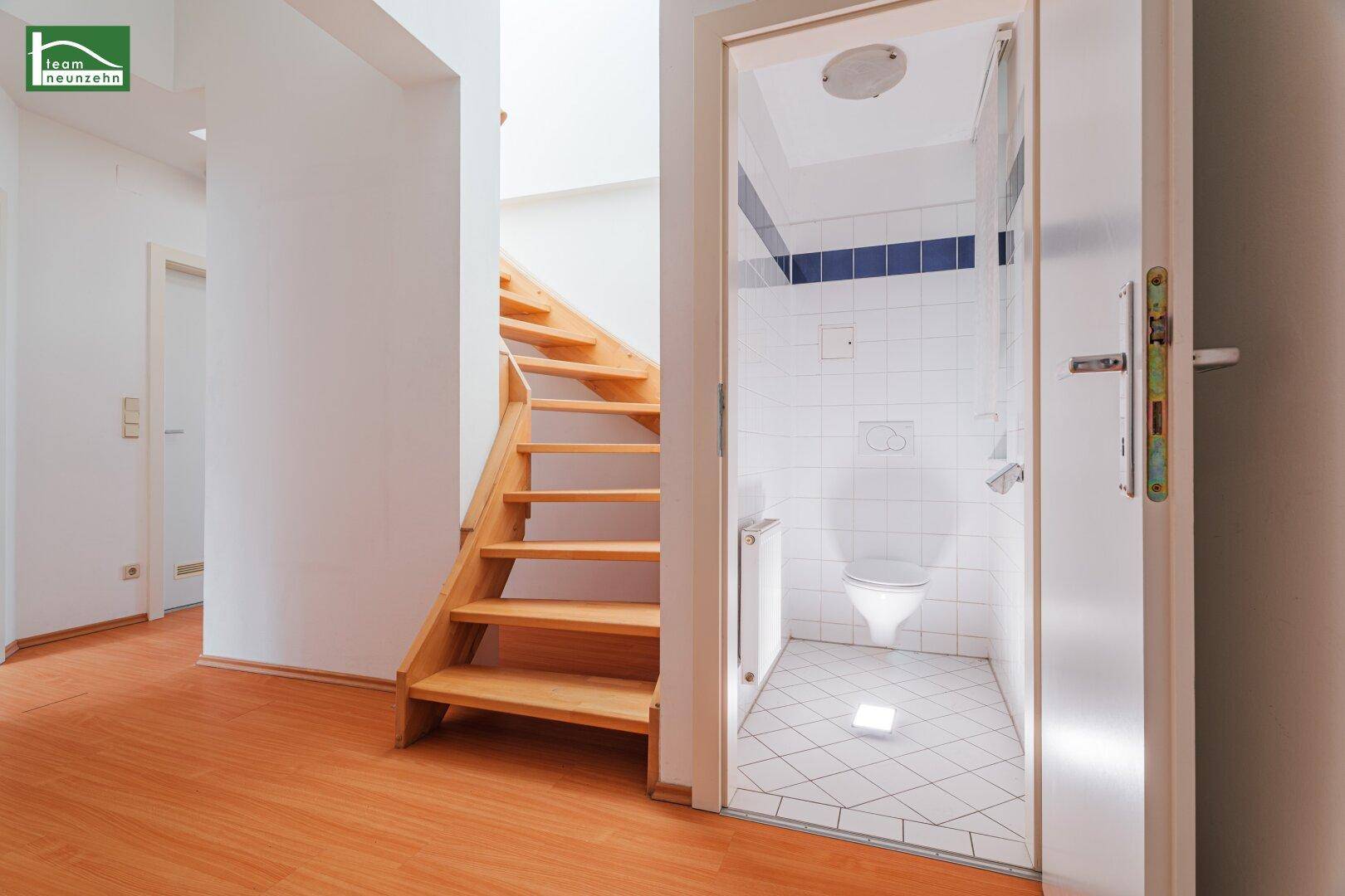 Flur mit Zugang zu einer kleinen Gästetoilette mit weißen Fliesen und WC.