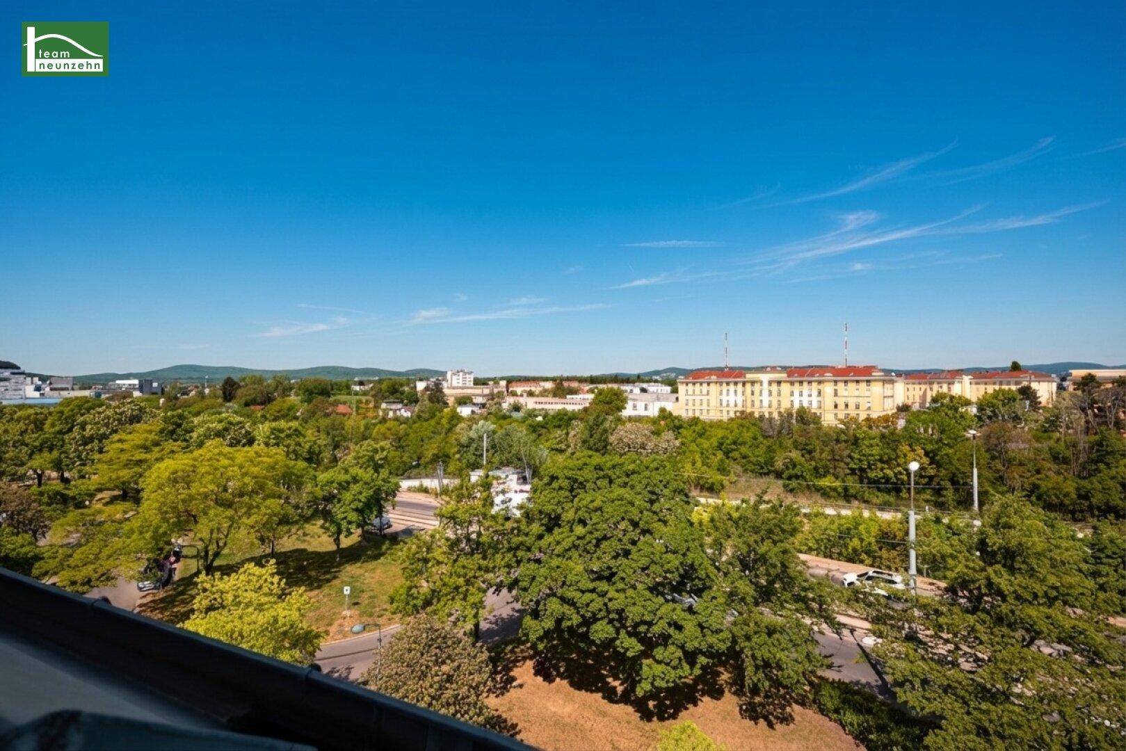 Weitläufiger Blick über die Stadt mit viel Grün und Gebäuden unter blauem Himmel.