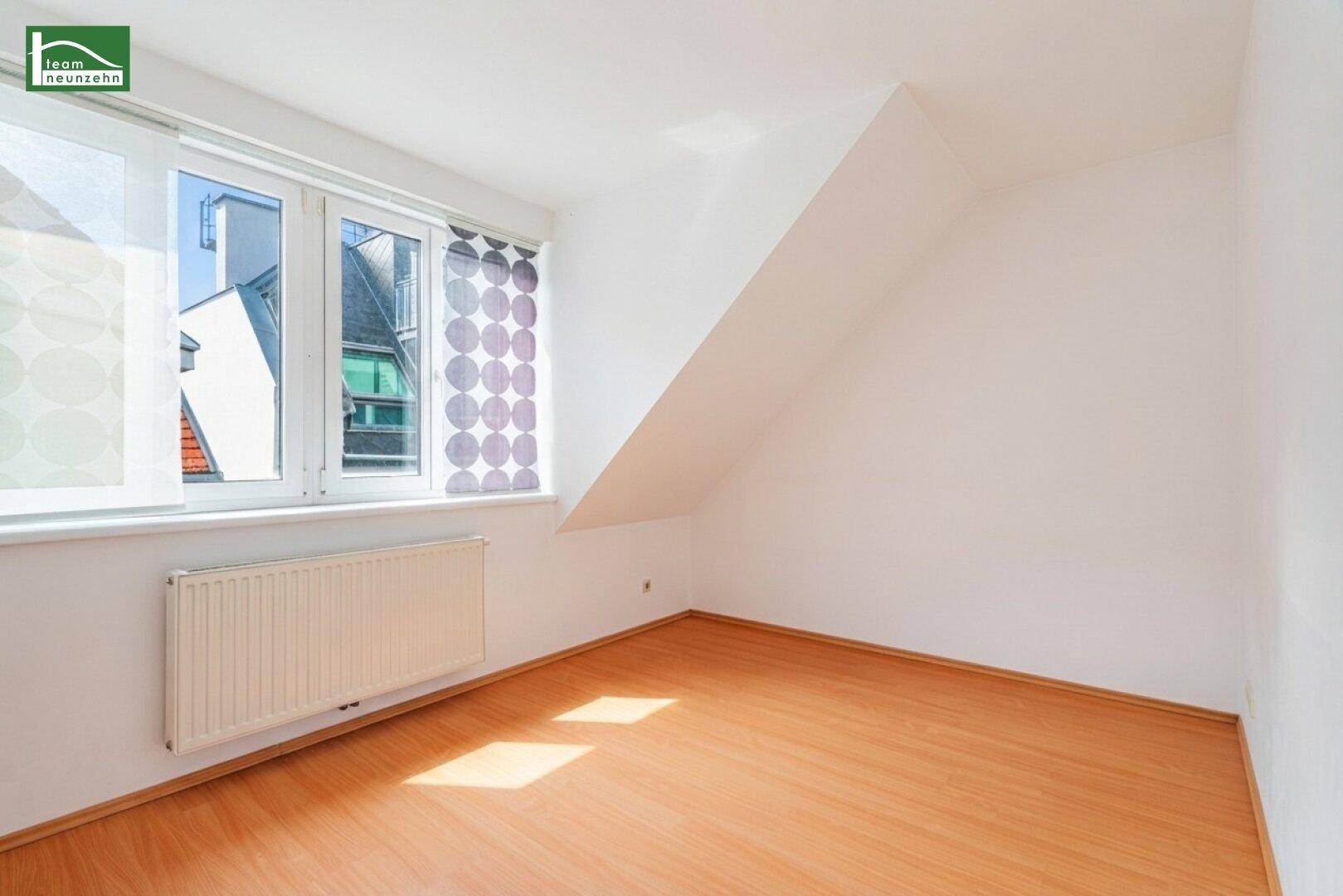 Helles Zimmer im Dachgeschoss mit Fenster, Schrägdecke und Holzfußboden.