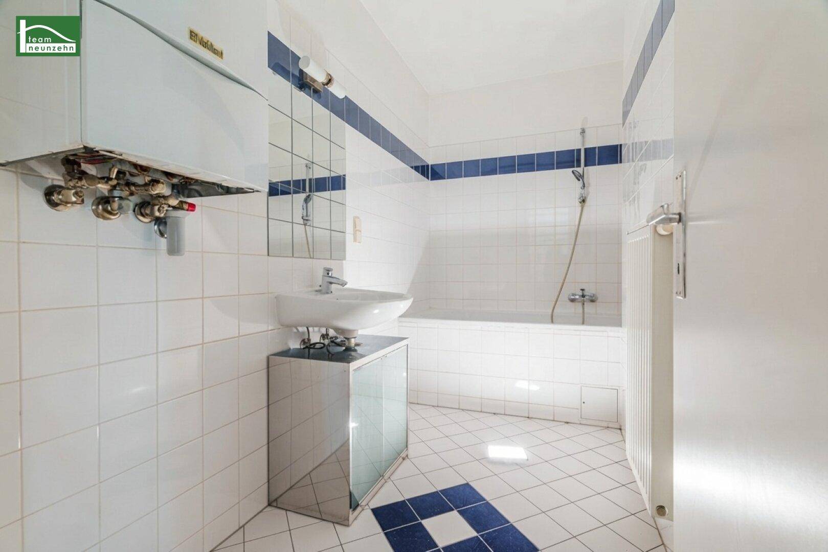 Gefliestes Badezimmer mit Badewanne, Waschbecken und blauen Akzenten.