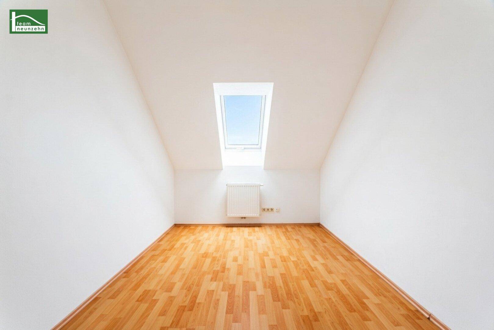Ruhiges Zimmer im Dachgeschoss mit Holzboden, weiß gestrichenen Wänden und einem Dachfenster.
