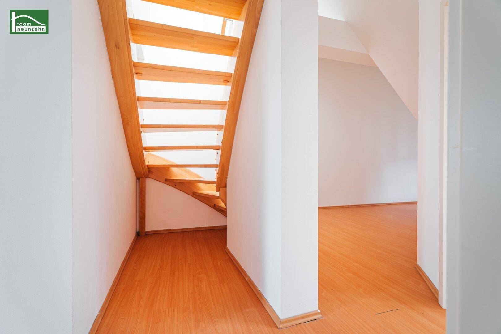 Heller Flurbereich mit Holztreppe, die in ein weiteres Stockwerk führt, und Holzboden.