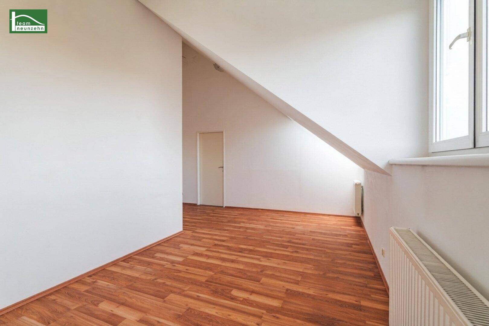 Heller Innenraum mit Holzboden und schrägen Wänden im Dachgeschoss, unmöbliert und leer.