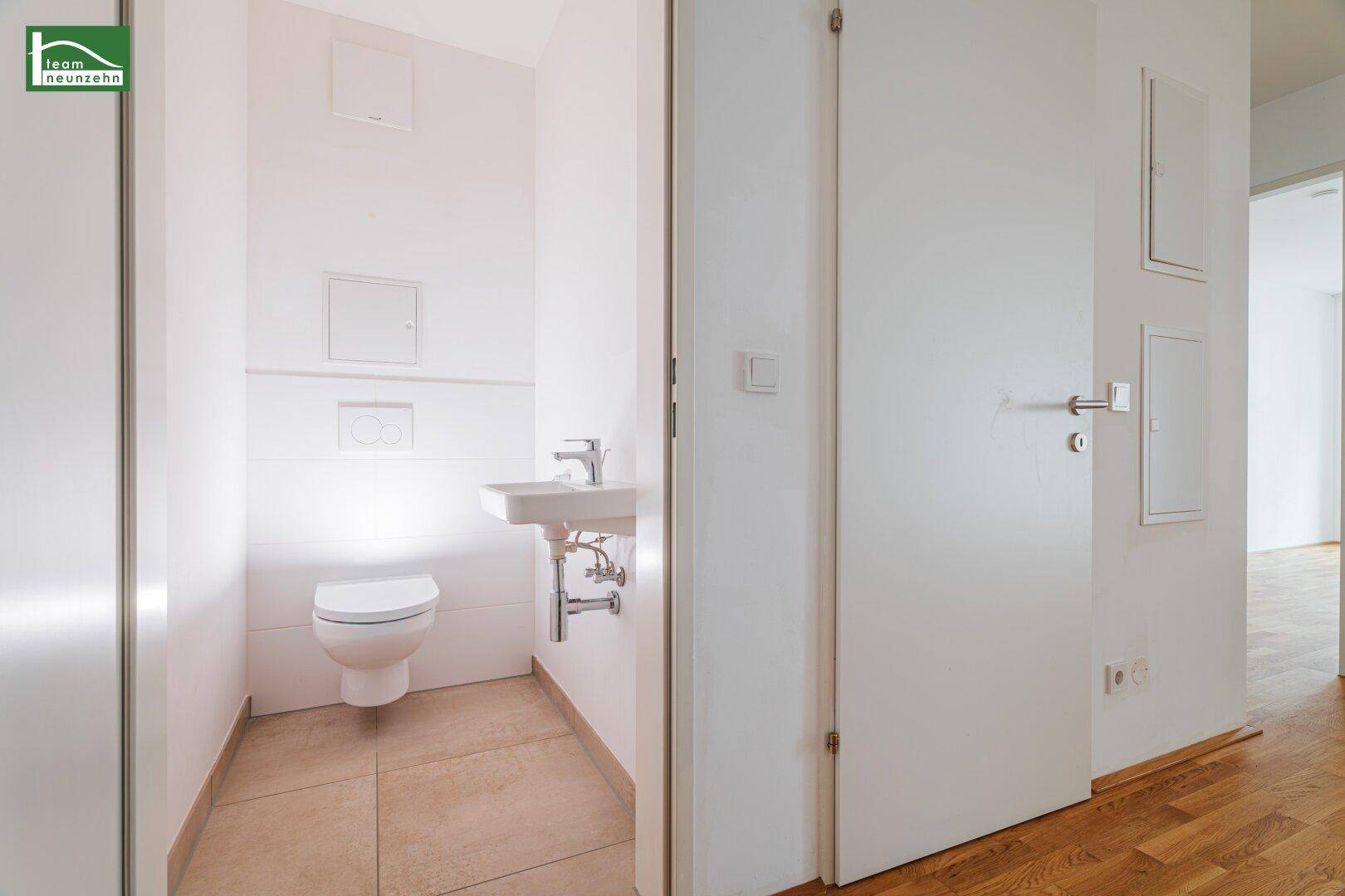 Separates Gäste-WC mit wandhängender Toilette und kleinem Waschbecken, hell gefliest und modern.