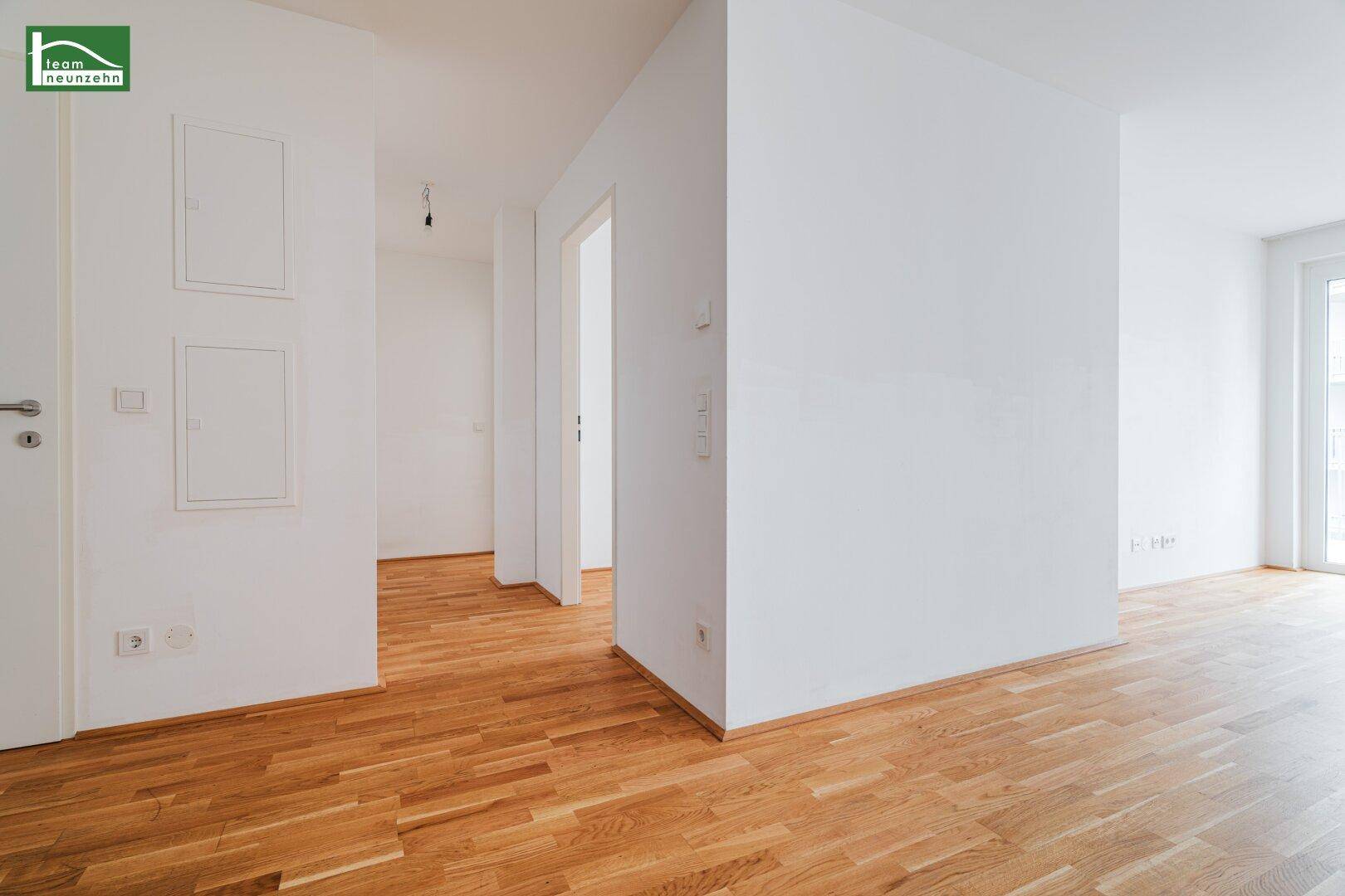 Heller Flur mit Parkettboden und weißen Wänden, der zu verschiedenen Räumen der Wohnung führt.