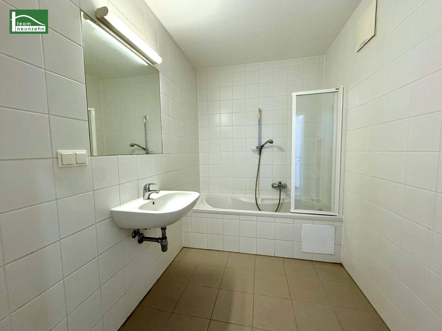 Gefliestes Badezimmer mit Badewanne, Duschabtrennung und Waschbecken.