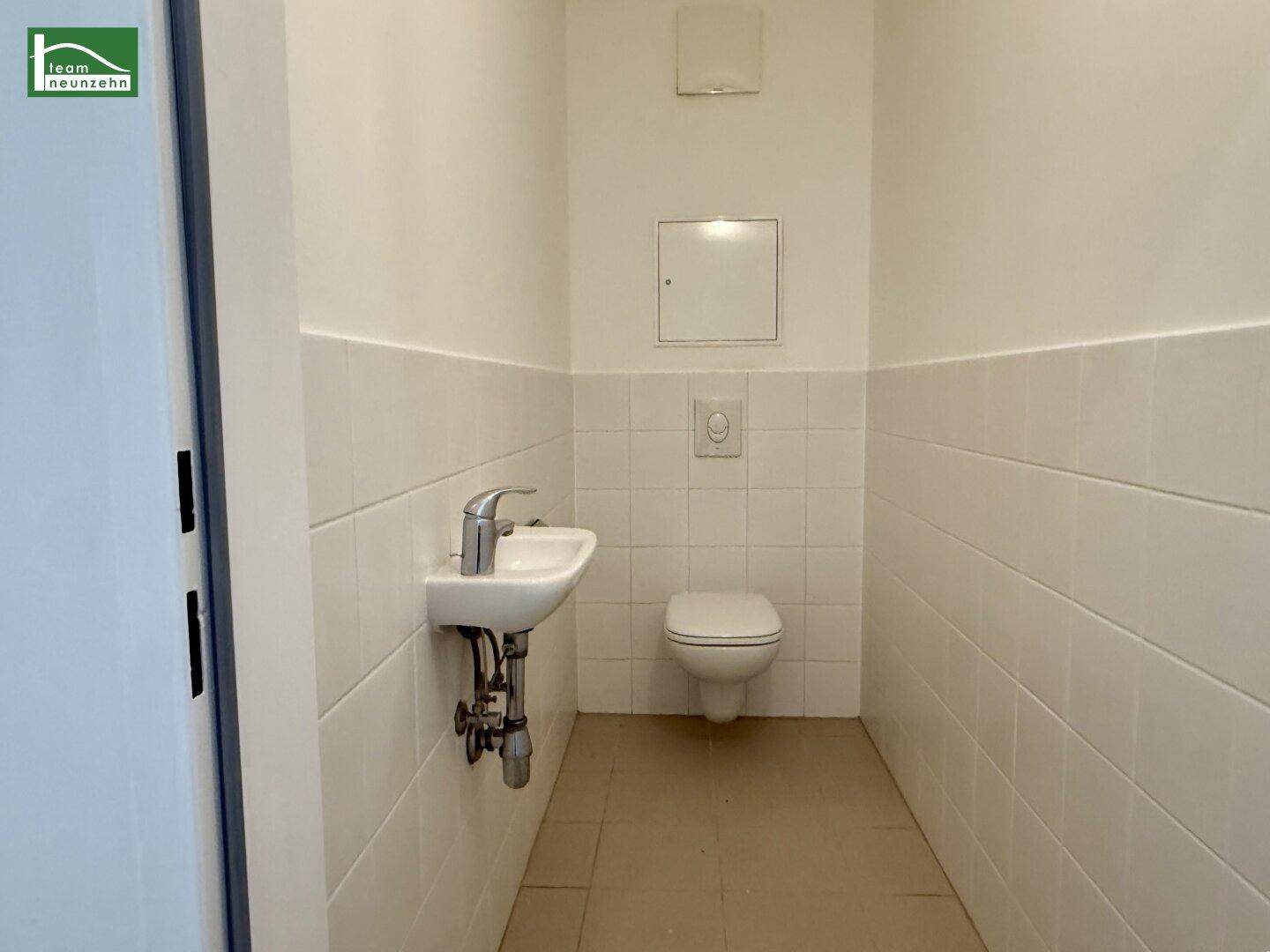 Separates WC mit Wand-WC, kleinem Waschbecken und weißen Fliesen.