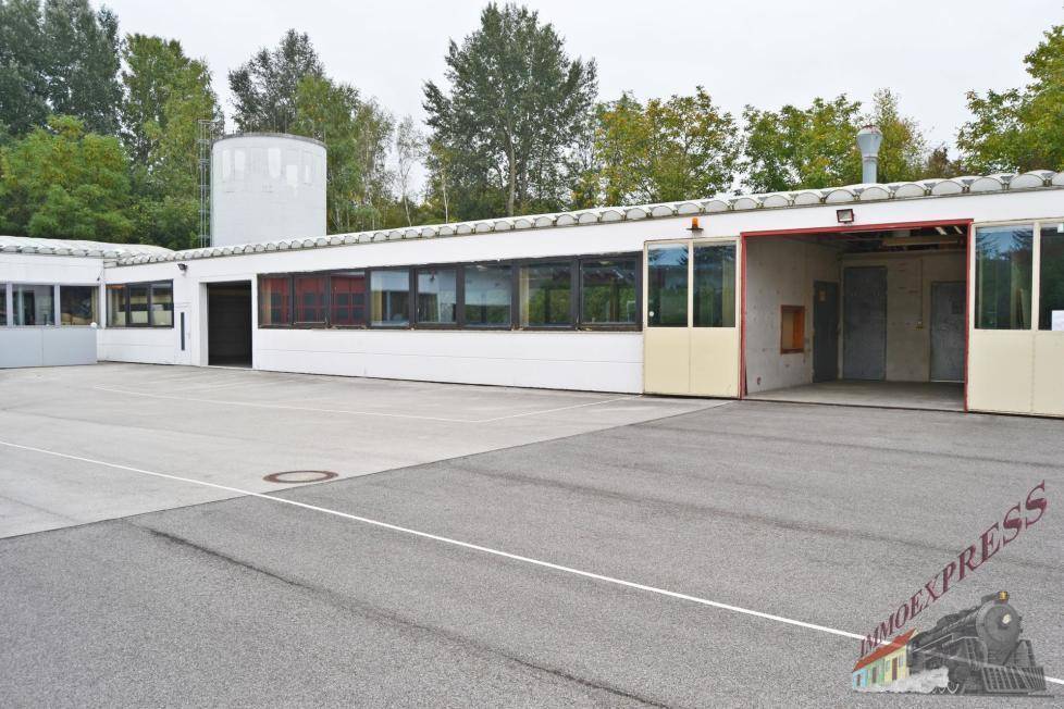 Gesamtansicht des Gewerbegebäudes mit ausgedehntem Parkplatz und umliegender Vegetation an einem hellen Tag.