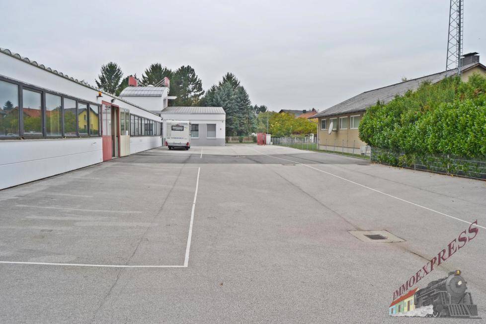 Weitläufiger Außenbereich des Gewerbeobjekts mit Parkplätzen und angrenzenden Gebäuden unter bewölktem Himmel.