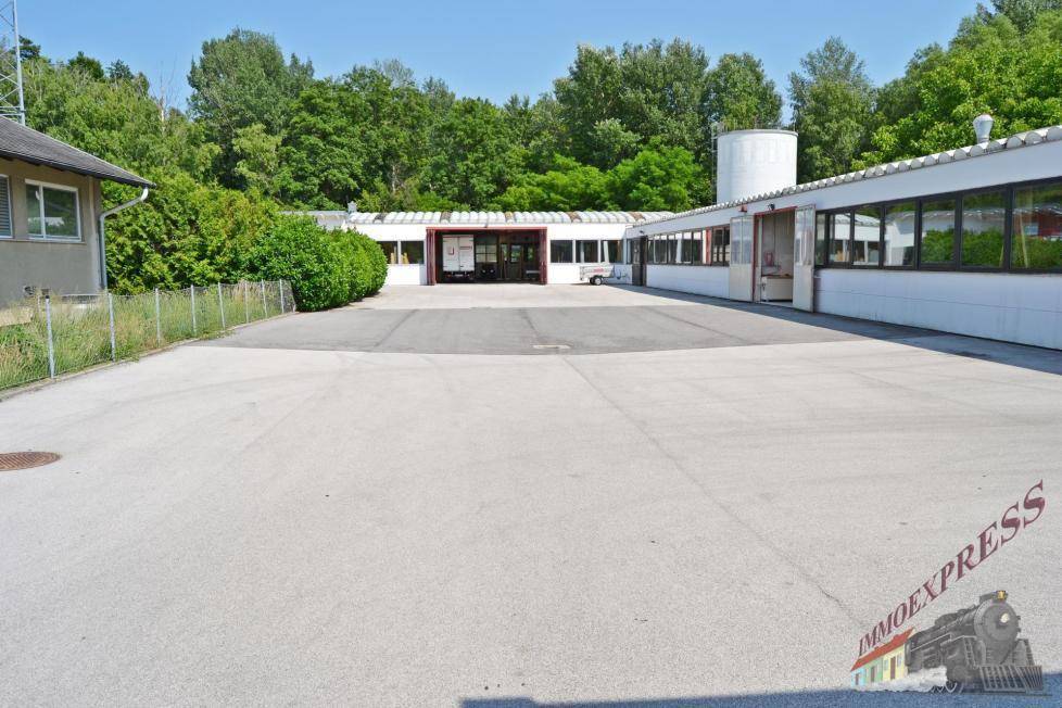 Gesamtansicht des Gewerbekomplexes mit weitläufigem Vorplatz und umgebender Grünfläche unter blauem Himmel.