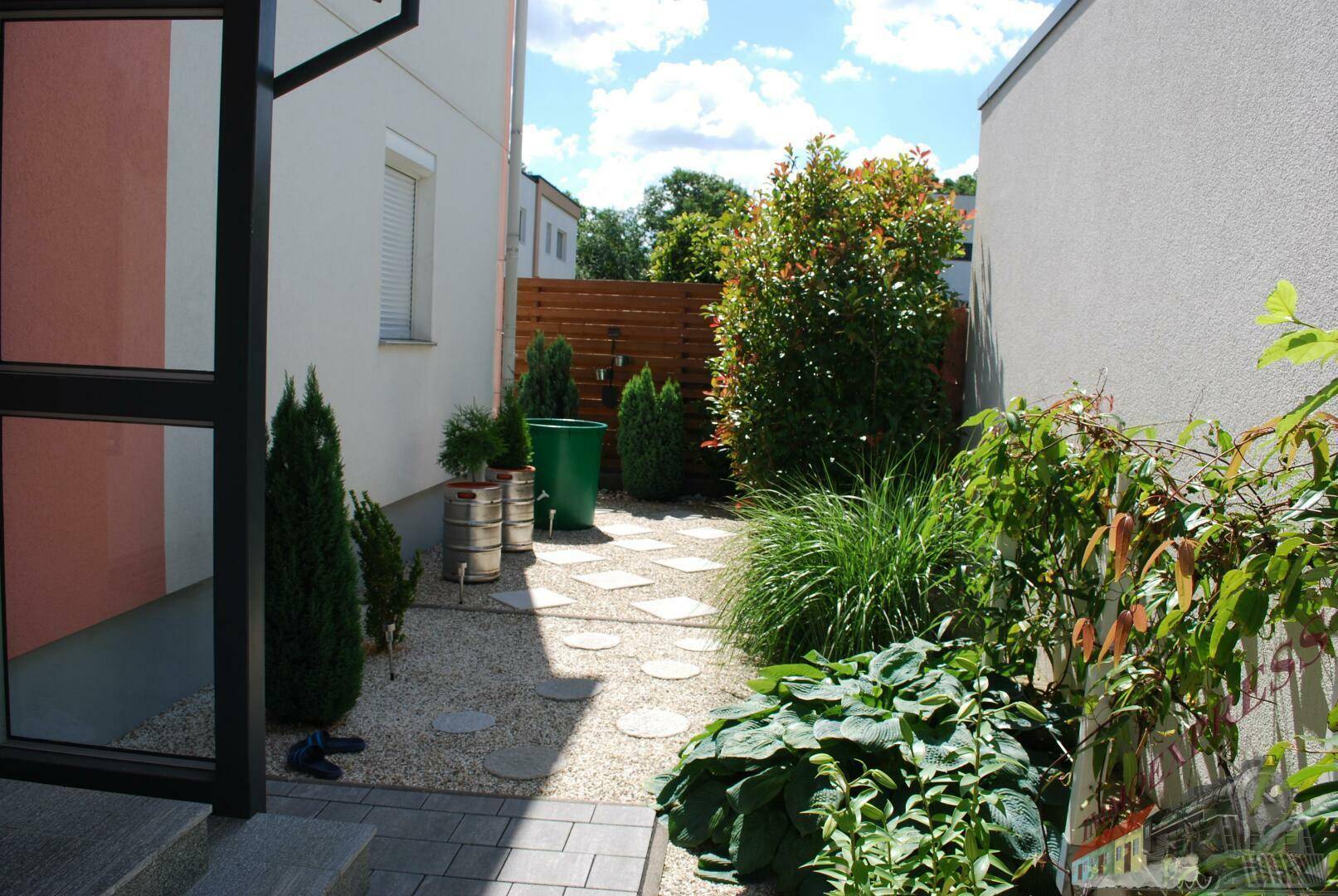 Seitlicher Zugang zum Haus mit Kiesweg, Trittplatten und grüner Bepflanzung.