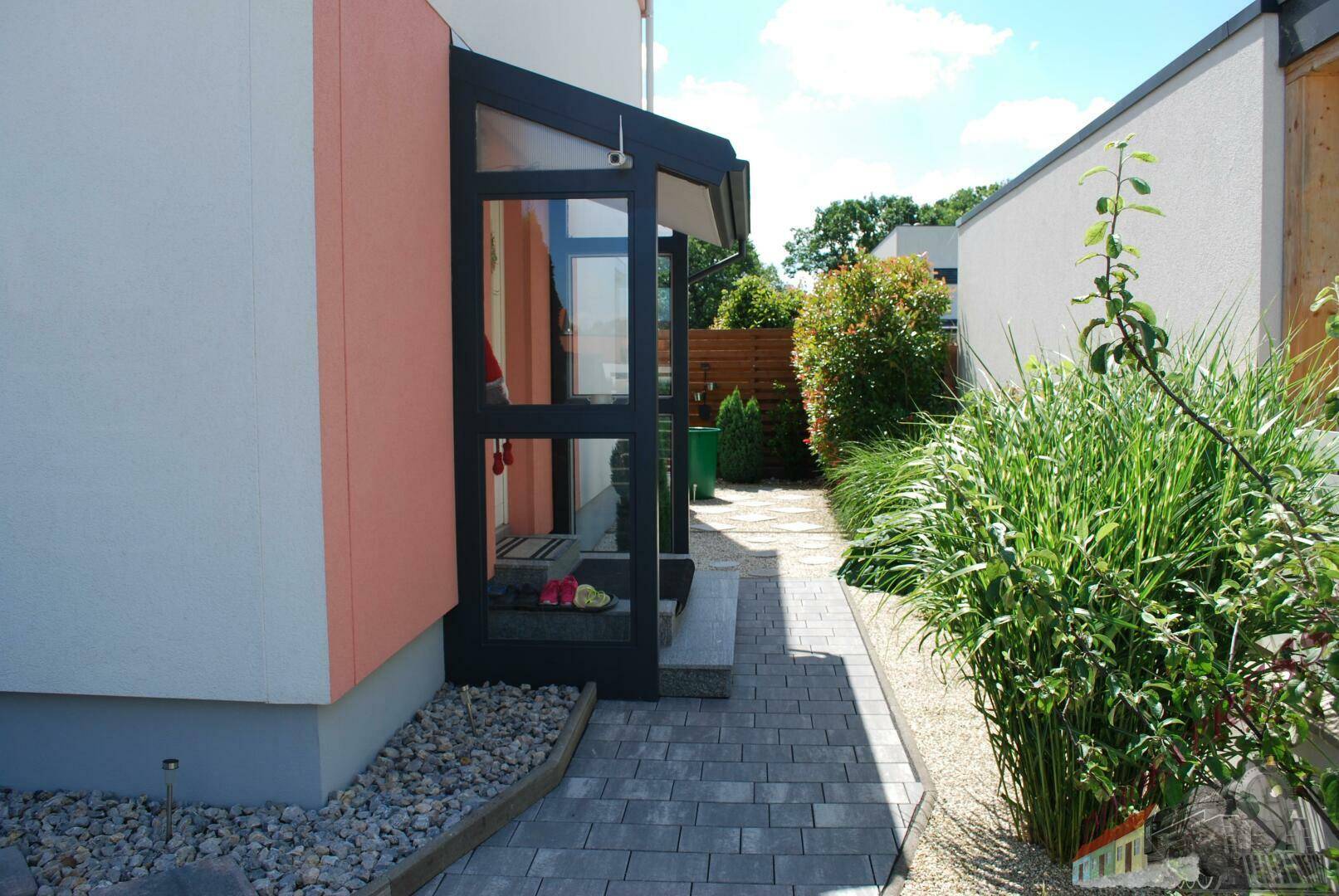 Seitlicher Zugang zum Haus mit gepflastertem Weg und üppiger Bepflanzung.