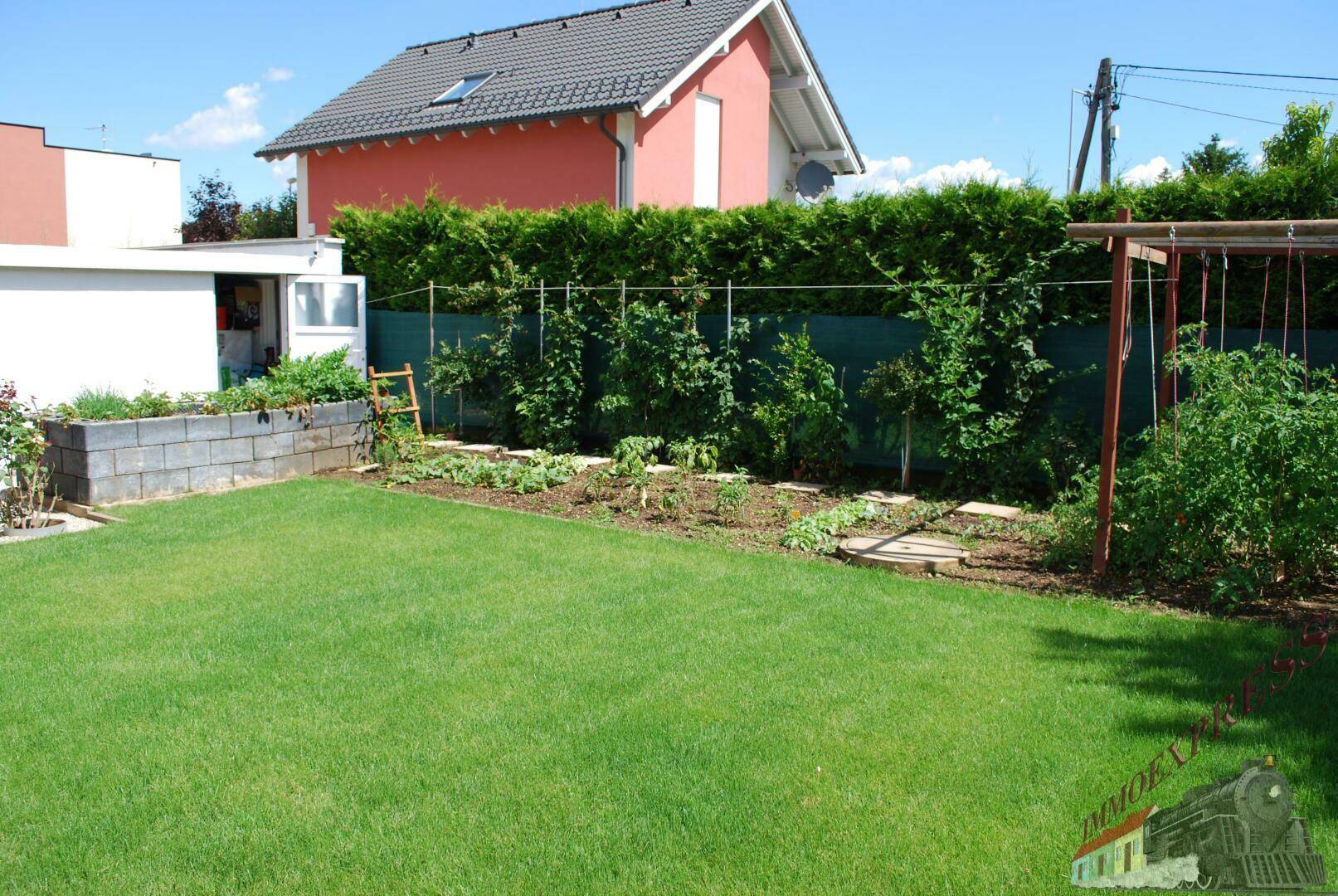Gartenbereich mit Rasenfläche, bepflanzten Hochbeeten und Hecke.