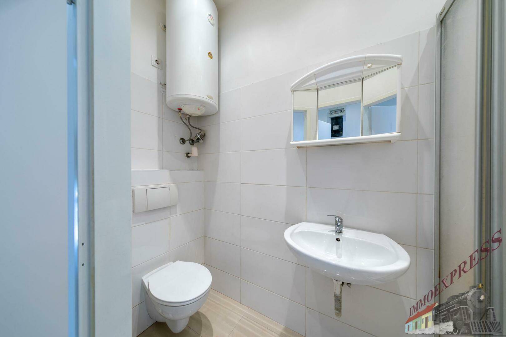 Kleines Badezimmer mit WC, Waschbecken, Spiegelschrank und Warmwasserboiler.