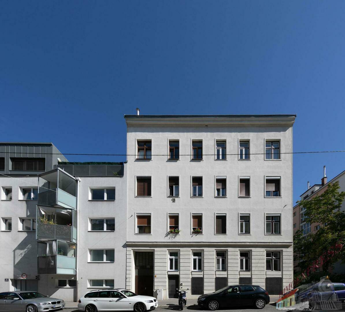 Mehrstöckiges Wohngebäude mit klassischer Fassade und geparkten Autos an einem sonnigen Tag.