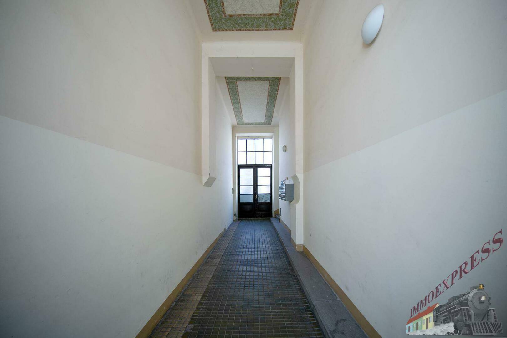 Langer Eingangsbereich mit Rampe und dekorierter Decke, der zum Hauptgebäude führt.
