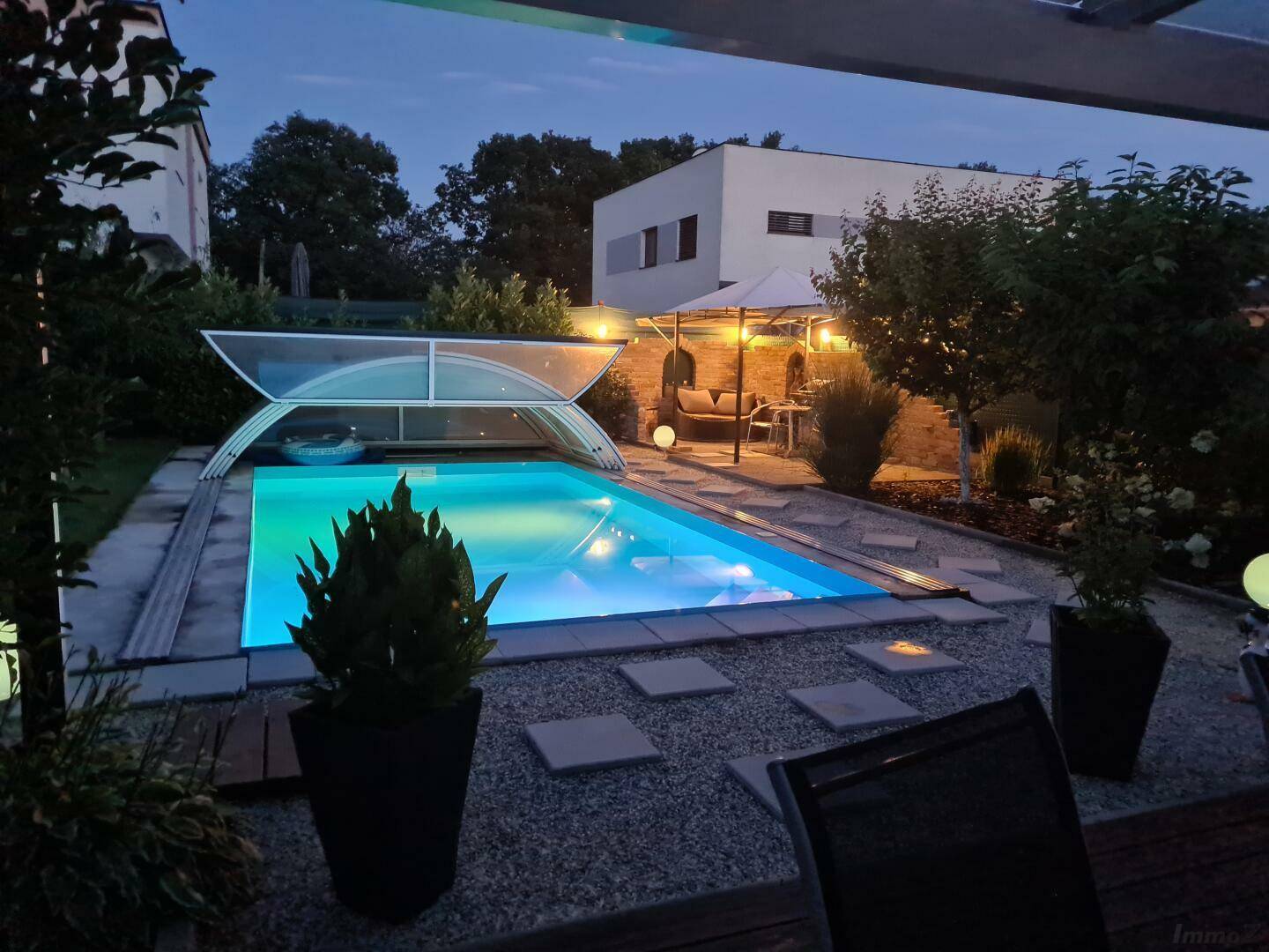 Beleuchteter Swimmingpool im Garten bei Nacht mit gemütlichem Sitzbereich.