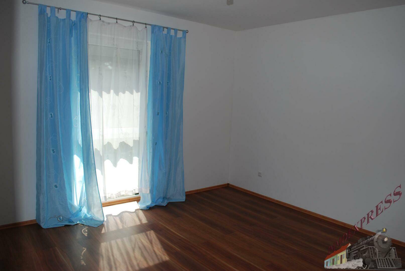 Helles Schlafzimmer mit Holzboden und großem Fenster mit blauen Vorhängen.