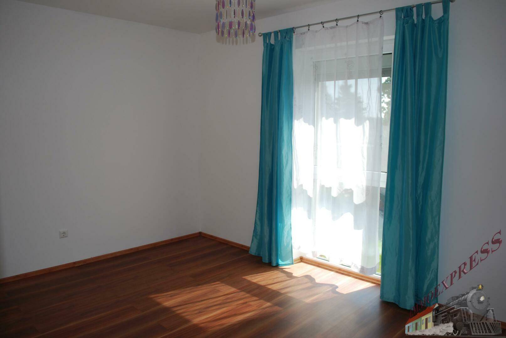 Helles Schlafzimmer mit Holzboden und großem Fenster mit türkisen Vorhängen.