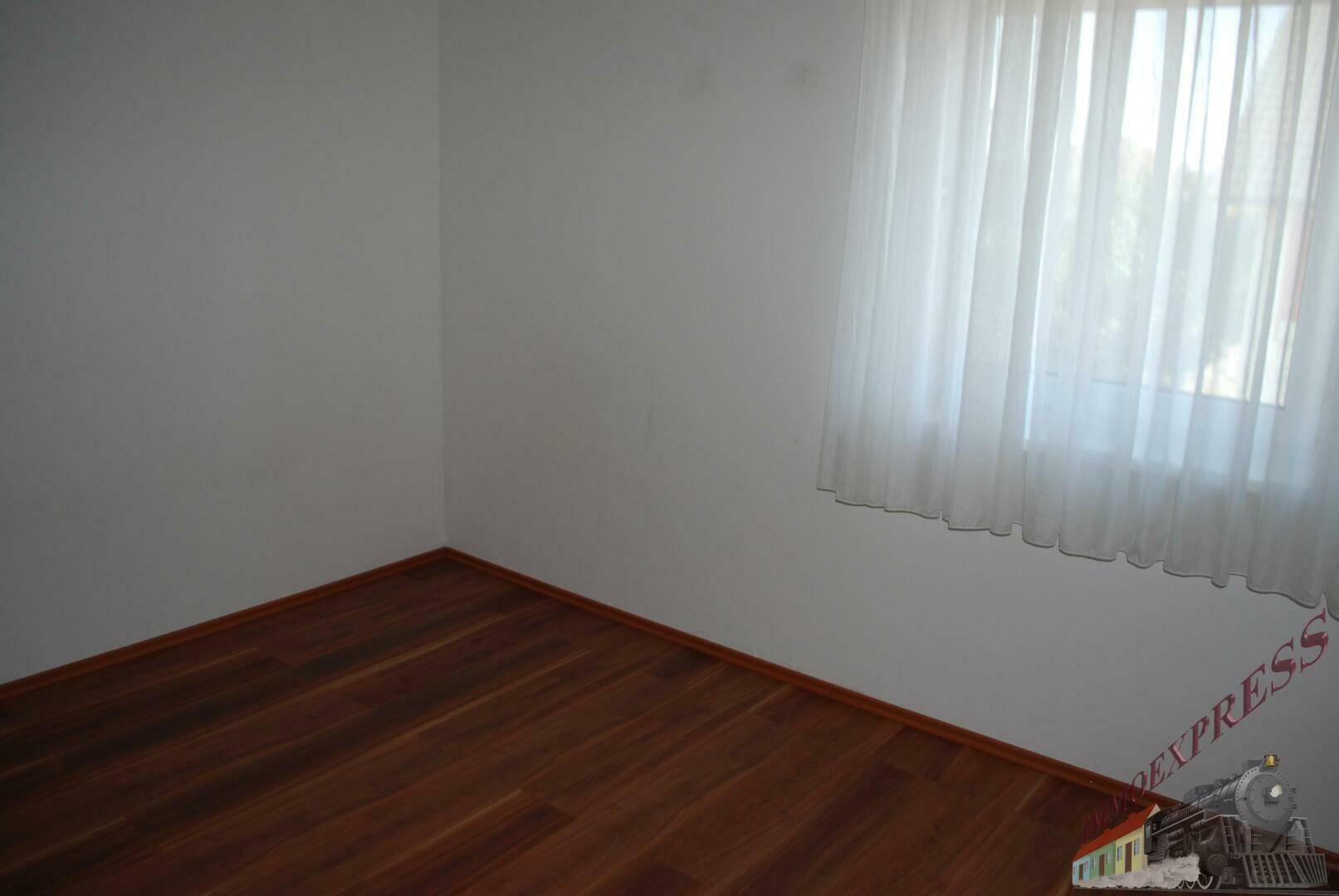 Helles Schlafzimmer mit Holzboden und Fenster mit weißen Gardinen.