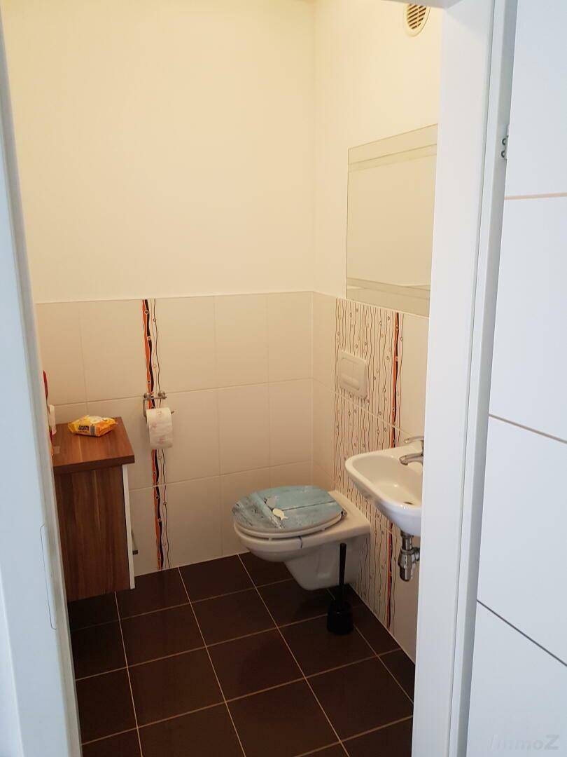 Modernes Gäste-WC mit Wand-WC, kleinem Waschbecken und Fliesen an Wänden und Boden.