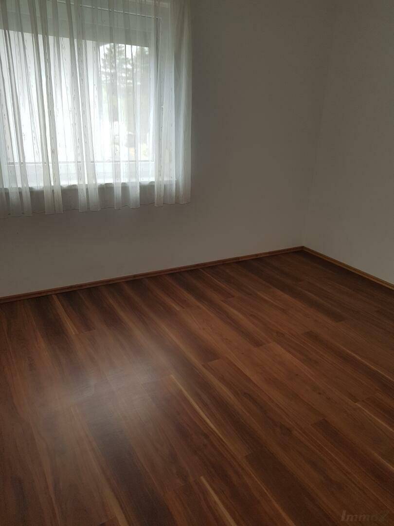 Helles Schlafzimmer mit Holzboden und Fenster mit weißen Gardinen.