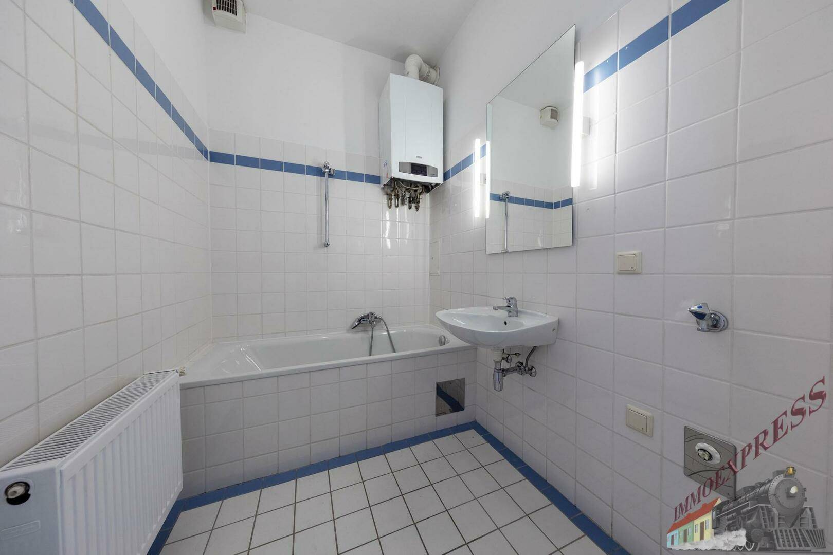 Badezimmer mit Badewanne, Waschbecken und weißen Fliesen mit blauen Akzenten.