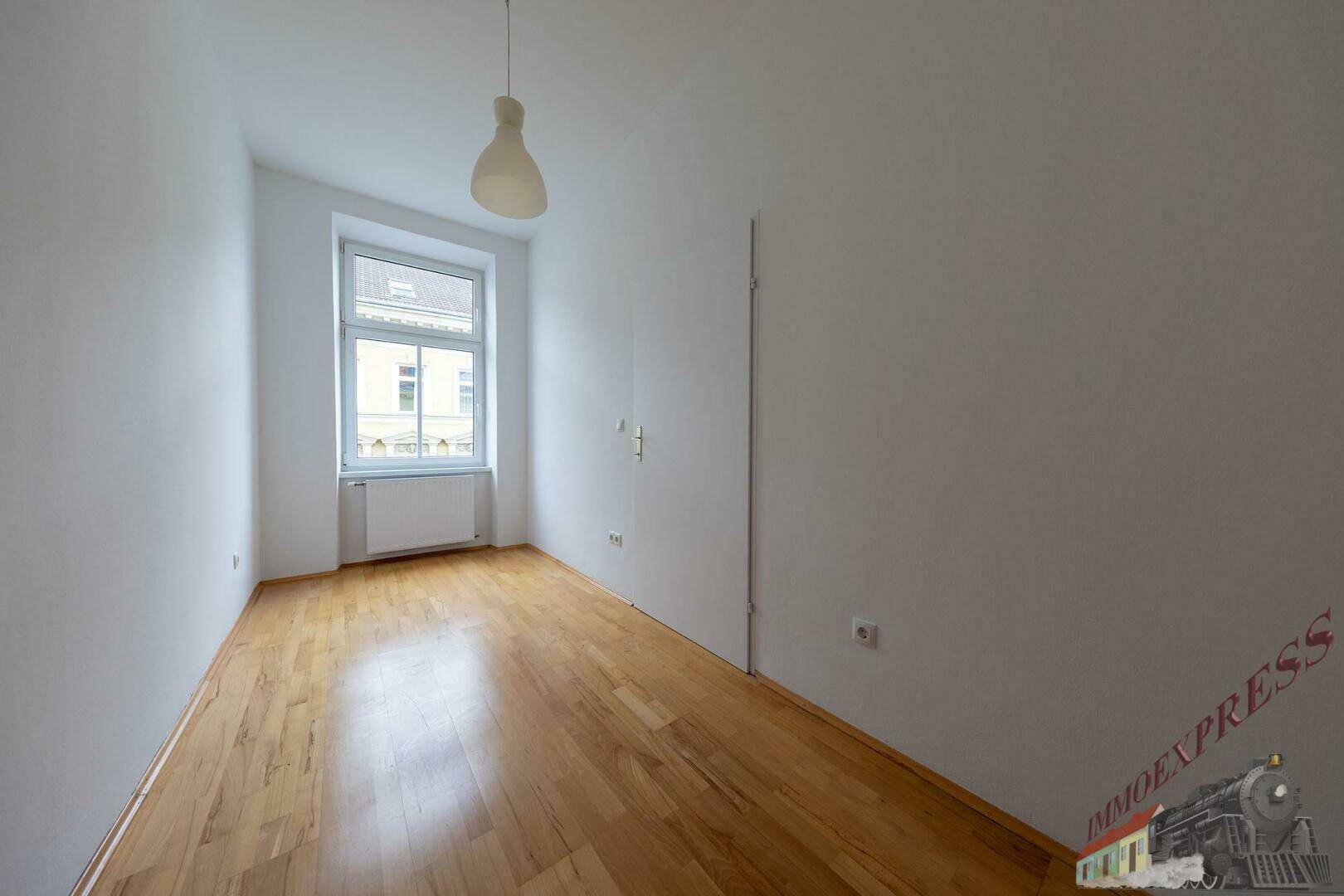 Helles Zimmer mit Parkettboden und einem Fenster, ideal als Schlaf- oder Arbeitszimmer.