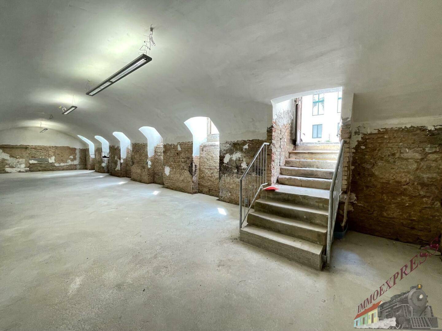 Geräumiger Kellerraum mit Gewölbedecke, unverputzten Wänden und einer Treppe zum oberen Bereich.