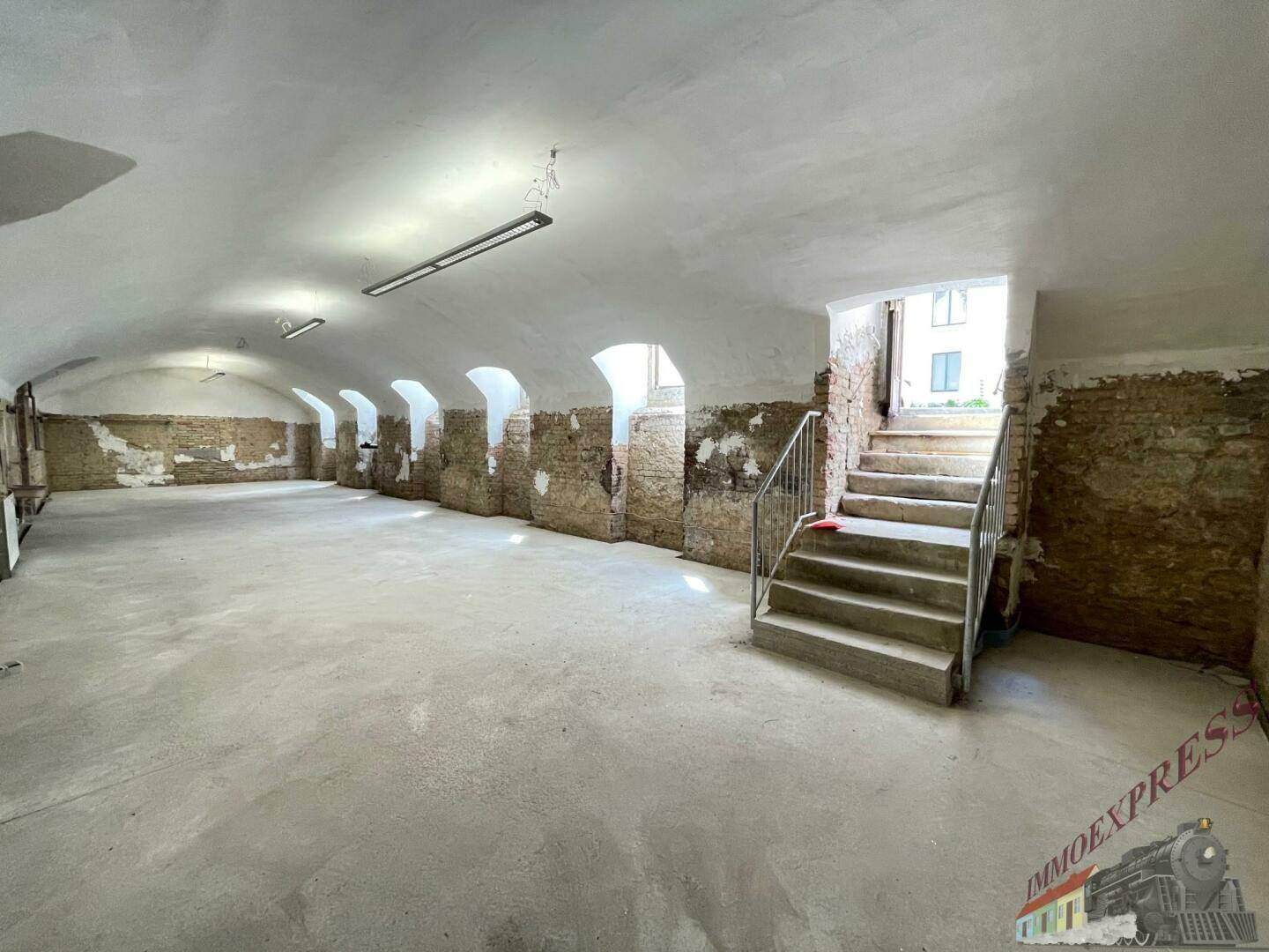 Geräumiger Kellerraum mit Gewölbedecke, unverputzten Wänden und einer Treppe zum oberen Bereich.