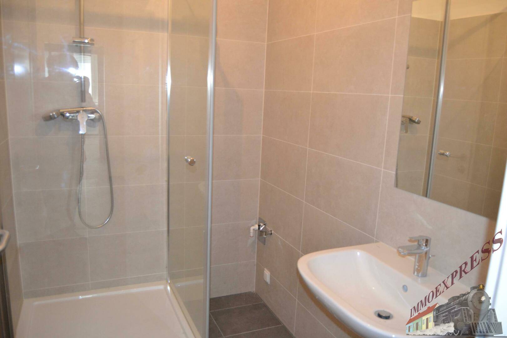 Modernes Badezimmer mit Duschkabine, Waschbecken und beigefarbenen Wand- und Bodenfliesen.