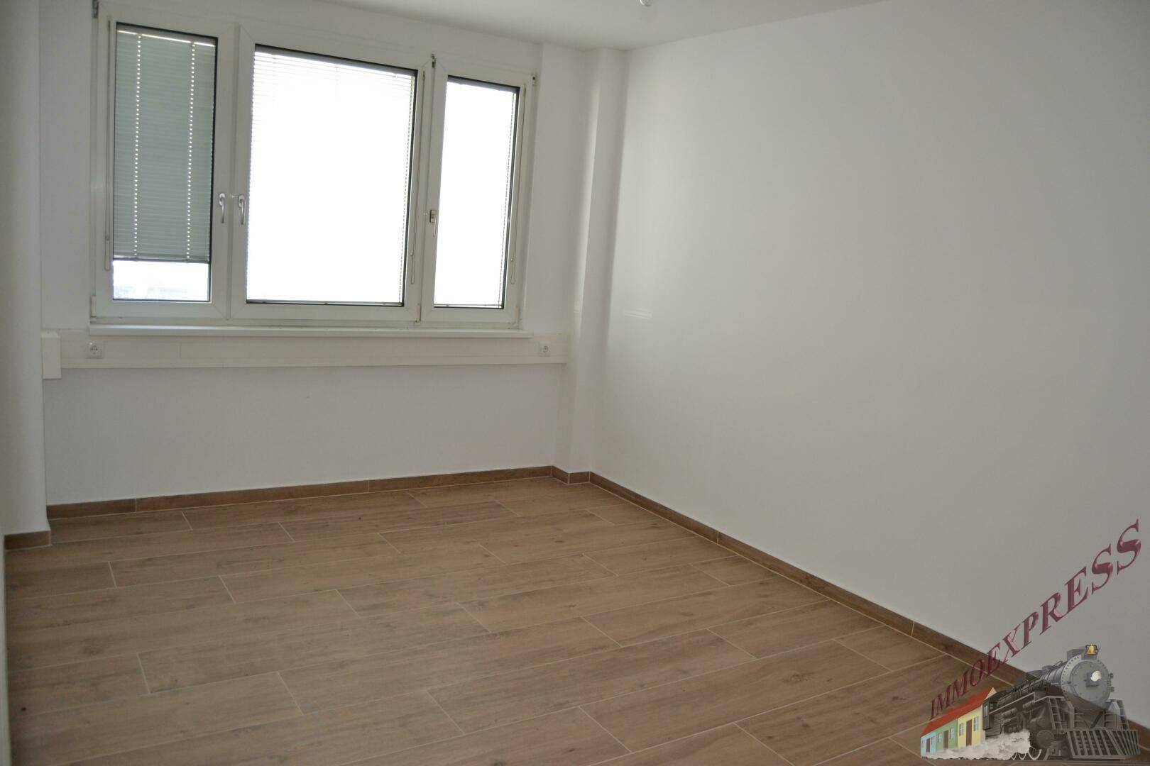 Kleinerer Büroraum mit einem großen Fenster und hellem Laminatboden, ideal für Einzelbüros.