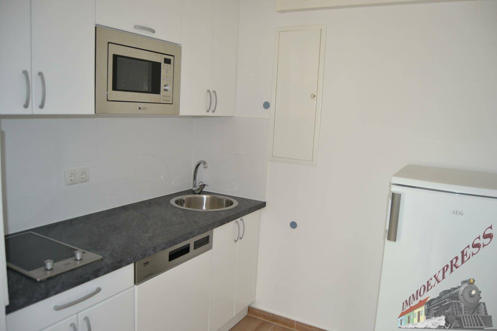 Kleine Einbauküche mit Mikrowelle, Spüle und Kochfeld, ideal für Büro oder Apartmentnutzung.