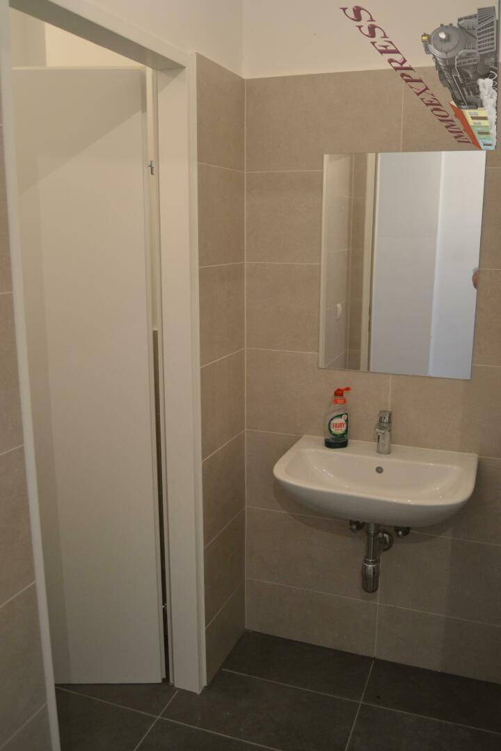 Modernes Badezimmer mit Waschbecken und Spiegel, hellen Fliesen und schlichter, funktionaler Einrichtung.