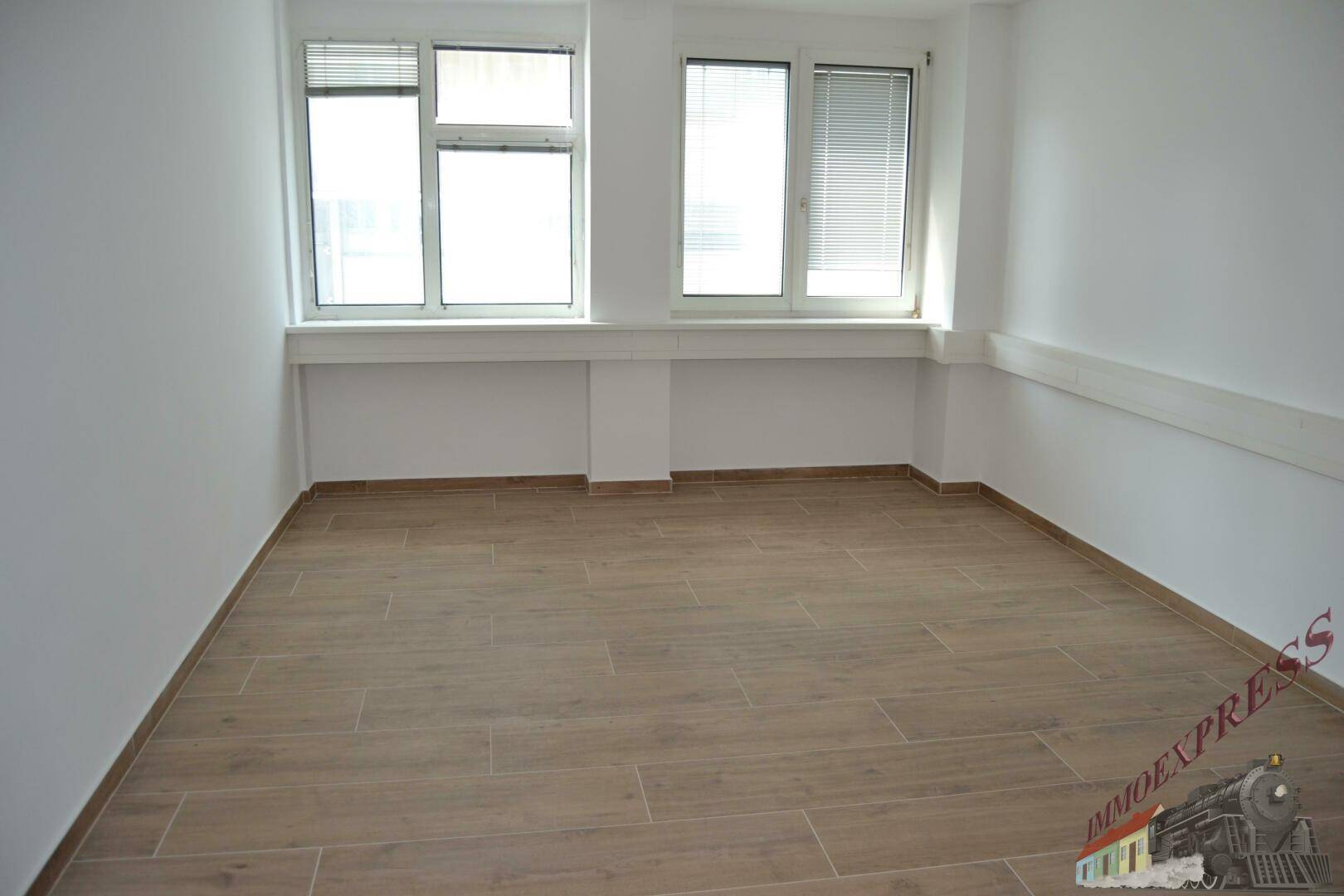 Leerer Büroraum mit zwei großen Fenstern und hellem Fliesenboden, bereit zur sofortigen Nutzung.