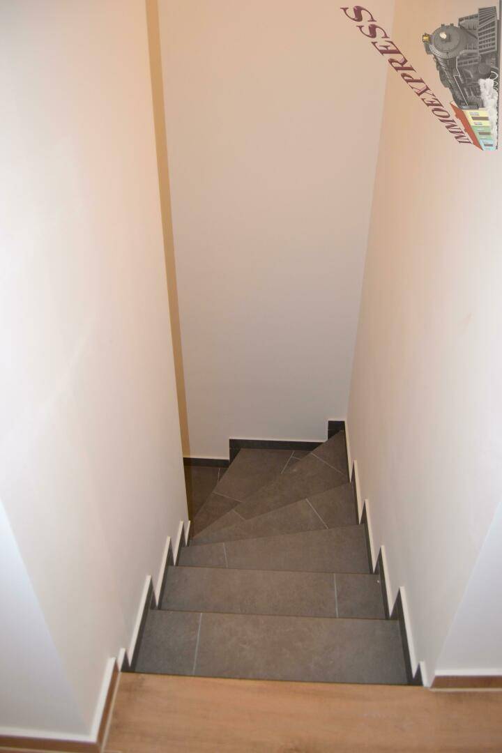 Treppenhaus mit gefliesten Stufen und schlichten Wänden, führt in die untere Etage des Gebäudes.