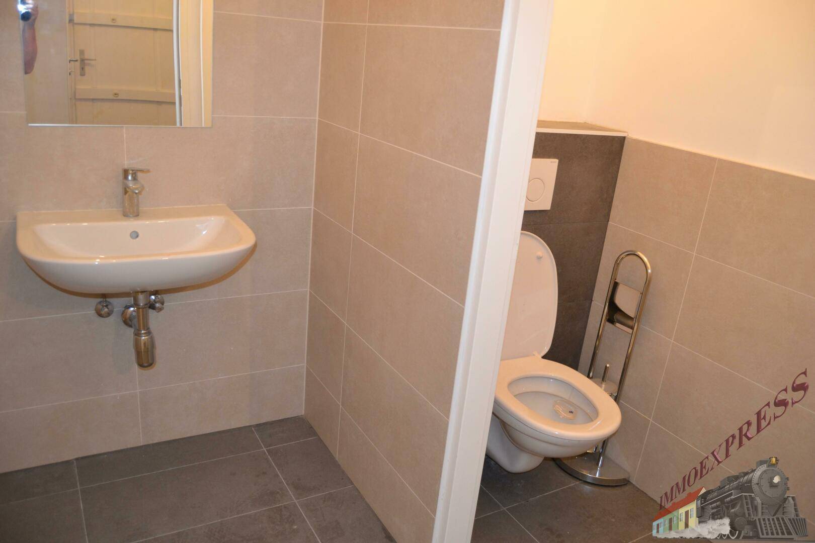 Separate Toilette mit Wand-WC, Waschbecken und modernen Fliesen, in neutralen Farbtönen gehalten.