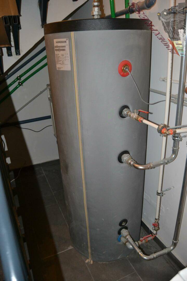 Großer Warmwasserspeicher in einem Technikraum, umgeben von Rohrleitungen und Installationen.