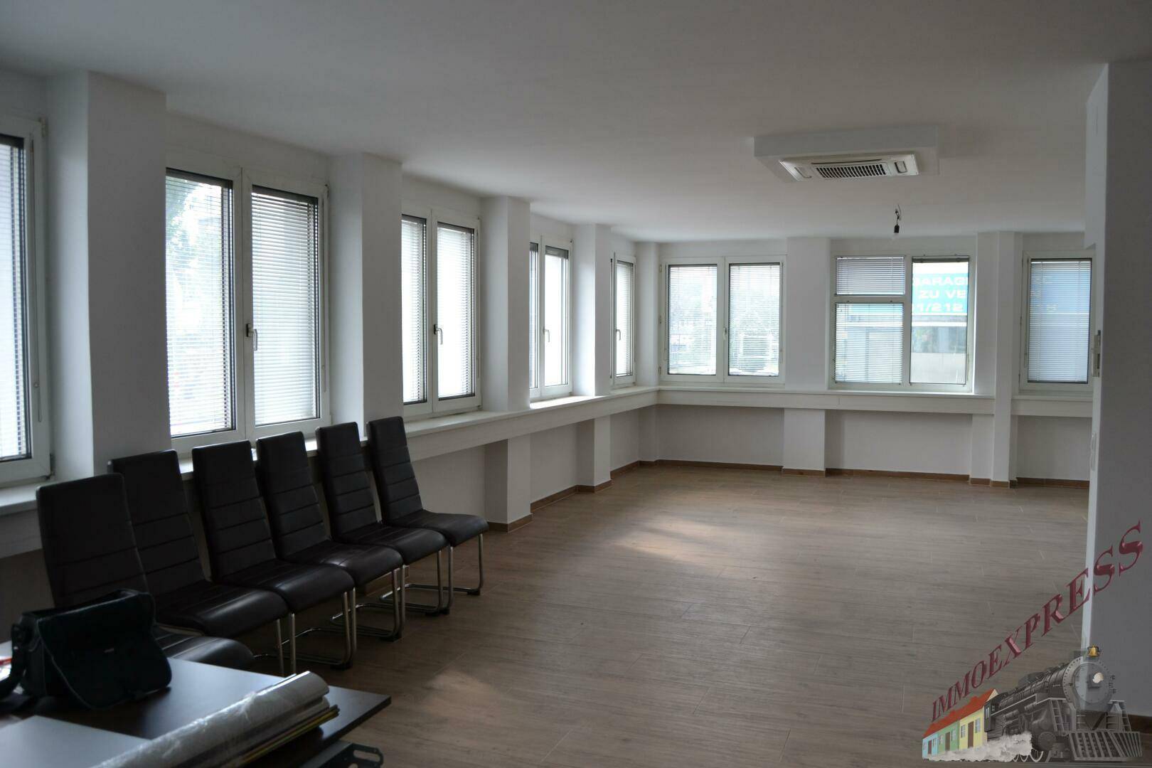 Großer, heller Büroraum mit vielen Fenstern, modernem Boden und Sitzgelegenheiten, ideal für Teamarbeit.
