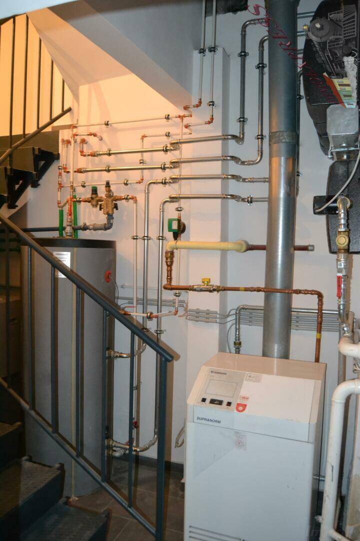Heizungsraum mit komplexer Rohrinstallation, Warmwasserspeicher und Heizkessel, gut gewartet.