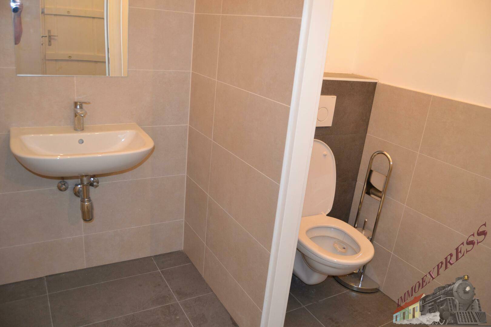 Separate Toilette mit Wand-WC, Waschbecken und modernen Fliesen in Grau- und Beigetönen.